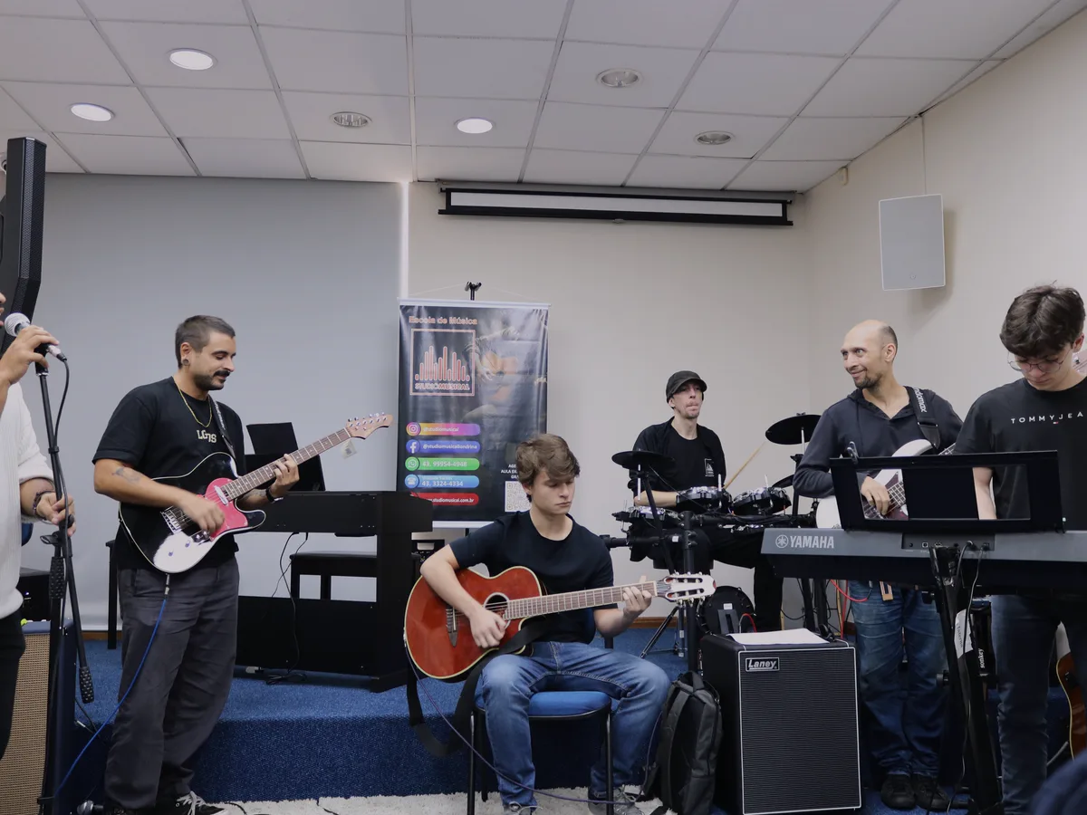 Aula de prática de banda no Studio Musical, com alunos no violão, no teclado e na bateria