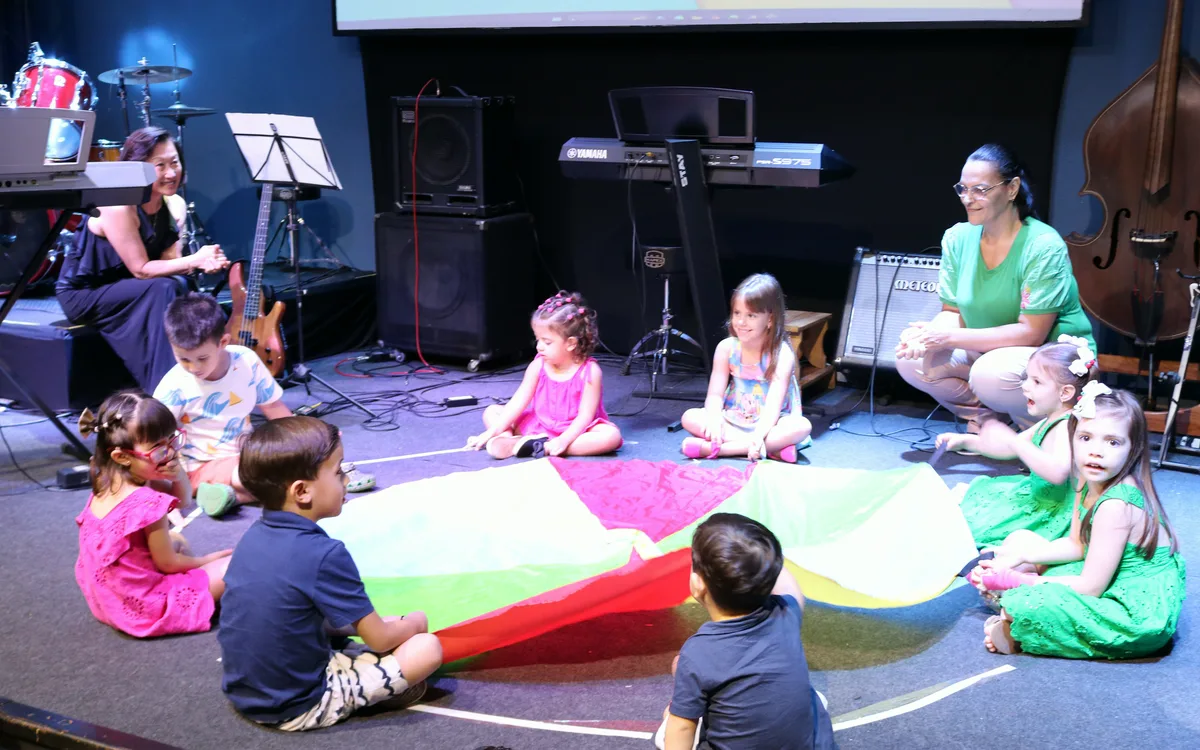 Roda de musicalização infantil no Studio Musical, com crianças sentadas em volta de um paraquedas colorido