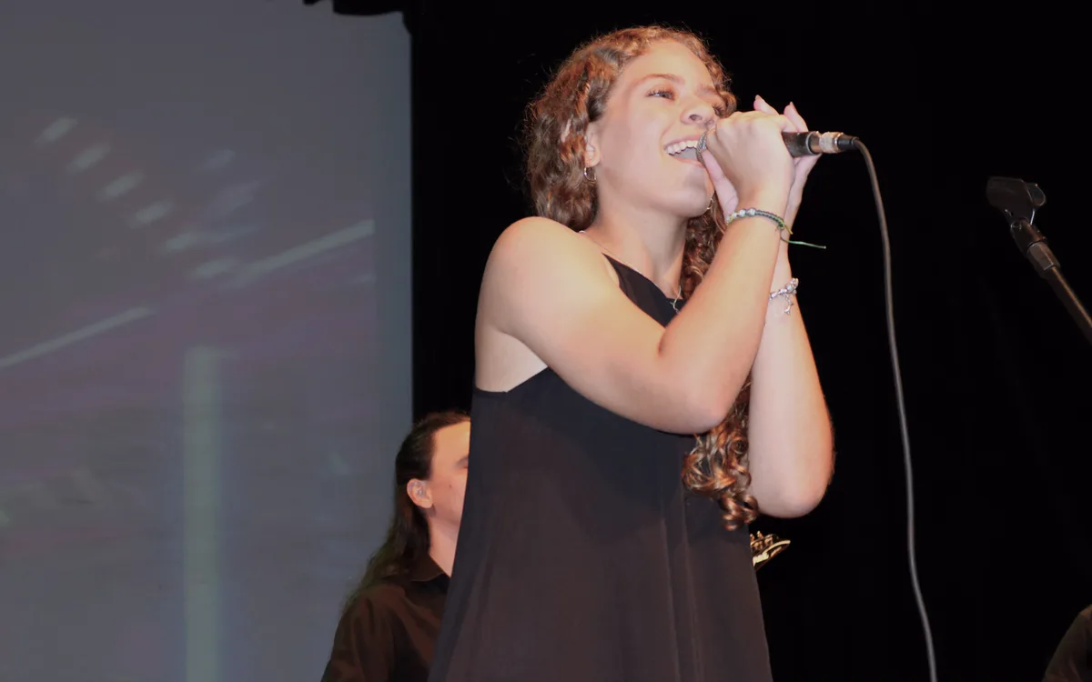 Aluna do Studio Musical cantando no palco durante apresentação da escola em Londrina